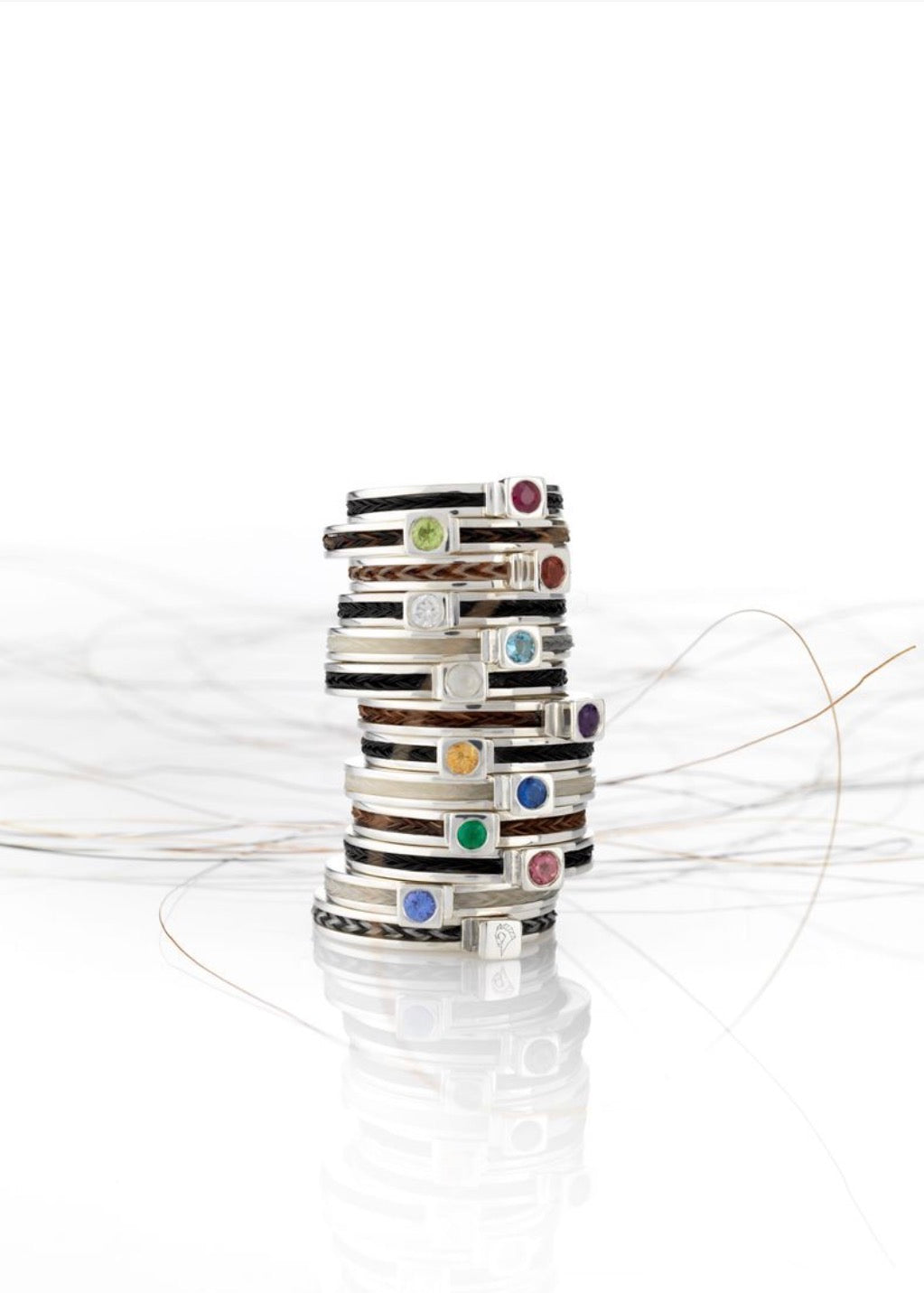 Stack of sterling silver Forged horse hair birthstone rings with braided black, chestnut and cream hair and colourful gemstones.