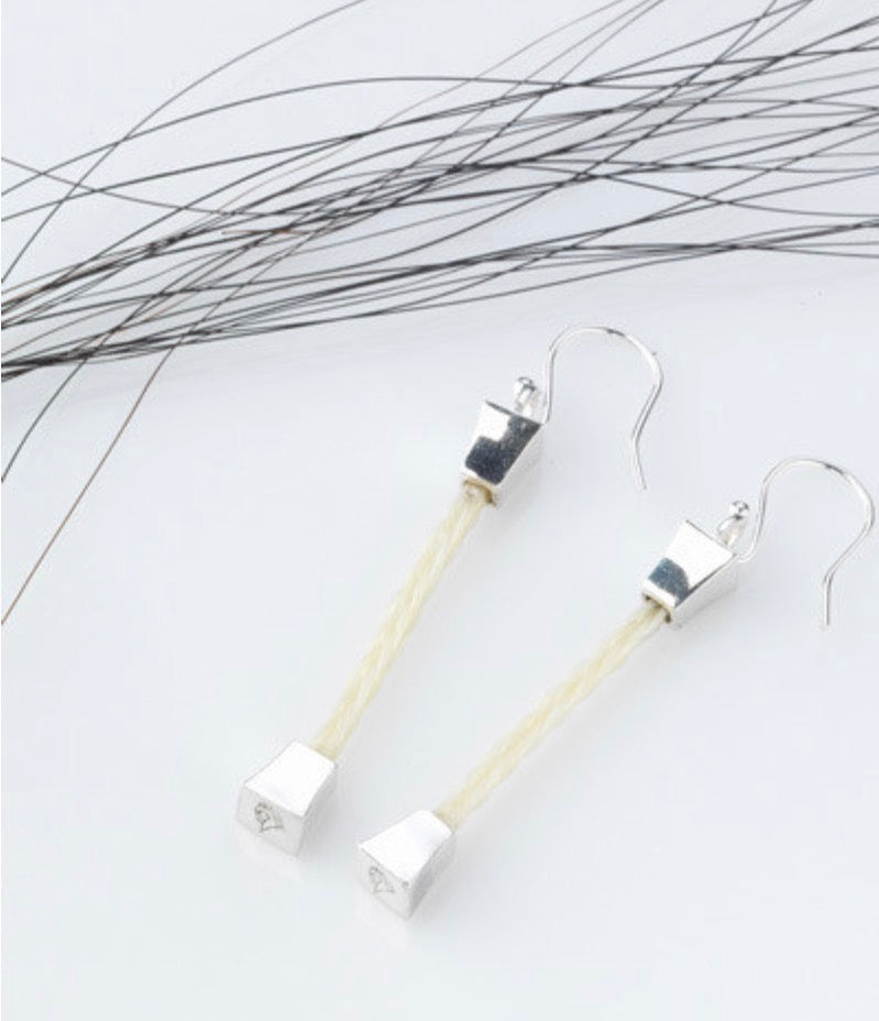 Close-up of the Forged Farriers Nail sterling silver drop earrings with cream square-braided horse hair and engraved horse-head end caps.