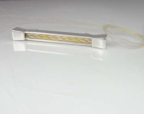 Forged Farriers Nail sterling silver pin with cream square-braided horse hair, displayed beside loose pale horse tail hairs.