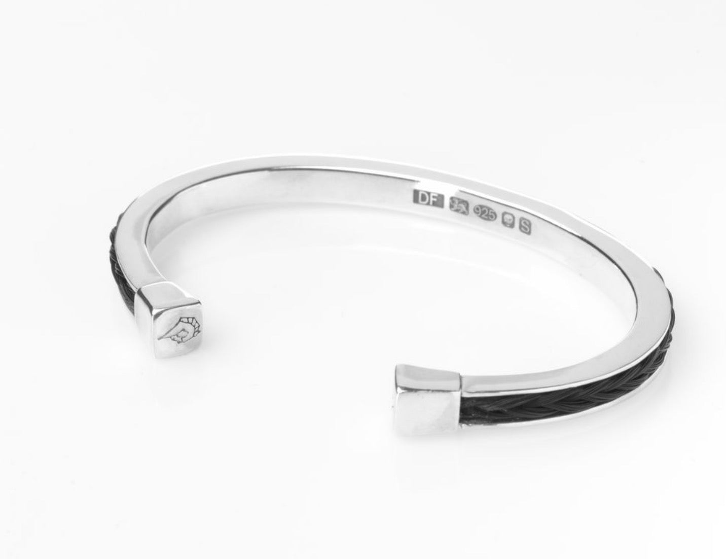 Three-quarter view of the Forged Farriers Nail sterling silver torque bangle with black braided horse hair inlay, visible hallmark and engraved end cap.
